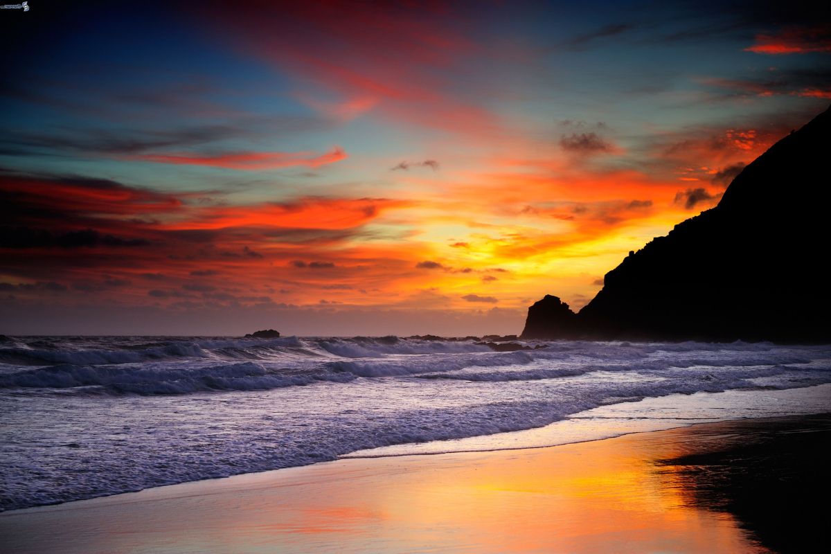 Vista panoramica al tramonto sulla spiaggia di Simius con il mare calmo, sabbia bianca e cielo colorato, barche in lontananza, atmosfera serena