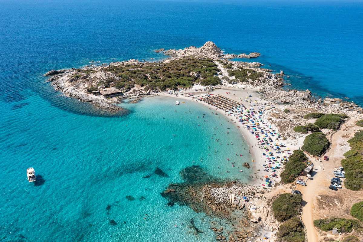 Vista aerea di Punta Molentis a Villasimius, spiaggia bianca, mare cristallino e promontorio roccioso, poche persone in acqua